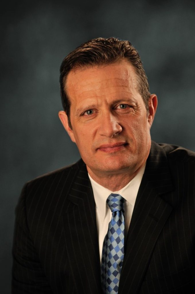 Portrait of a man in a striped suit and a blue patterned tie, facing forward with a neutral expression.