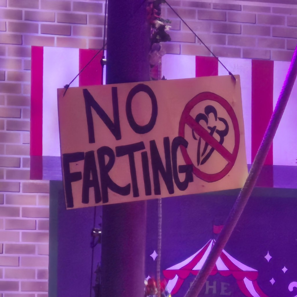 A sign reading 'No Farting' hangs at the entrance of Circus Flora, set against a colorful circus backdrop.