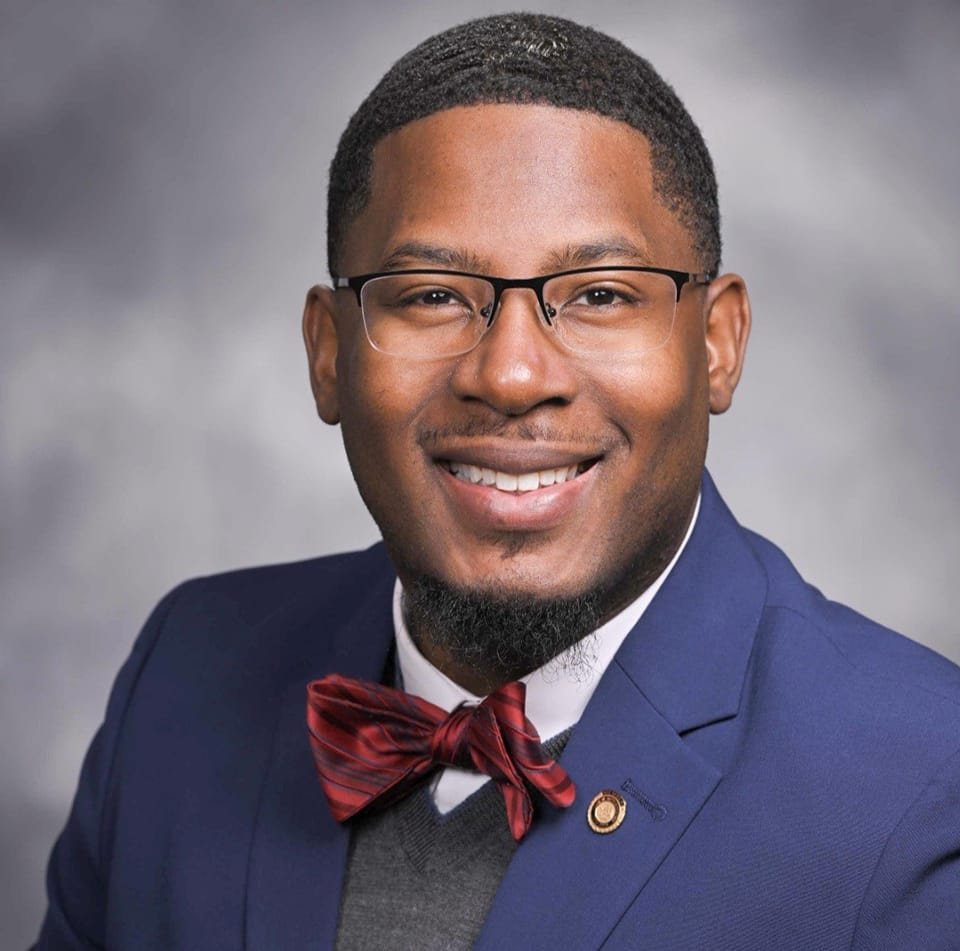 A smile portrait of Committeeman Shedrick Kelley, wearing a blue suit and red bow tie, posing for a professional photo.