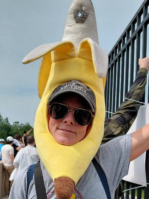 Person wearing a large banana hat at a protest, smiling and posing for the camera.