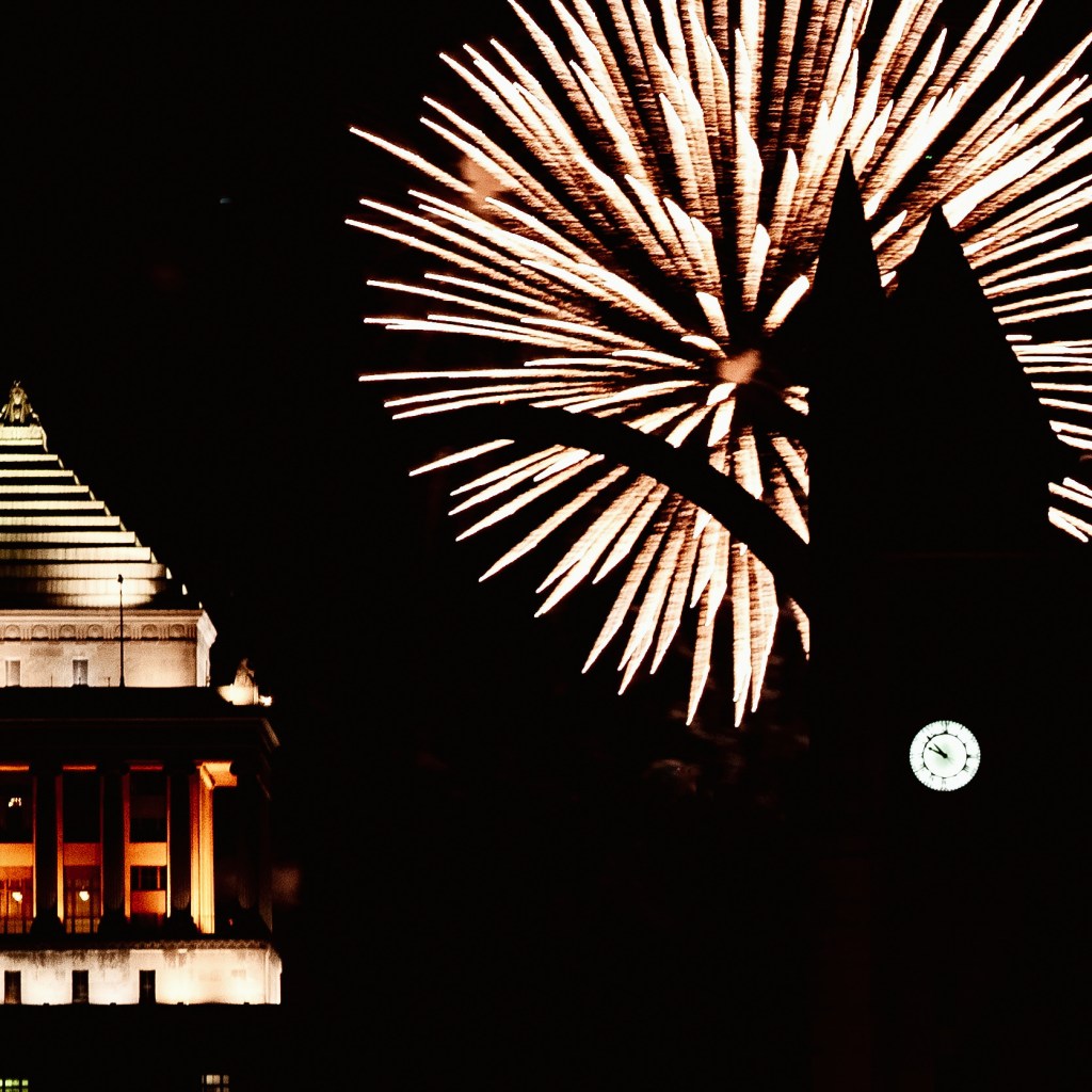 Fireworks illuminate the night sky behind a historic building, creating a festive atmosphere during a Fourth of July celebration.