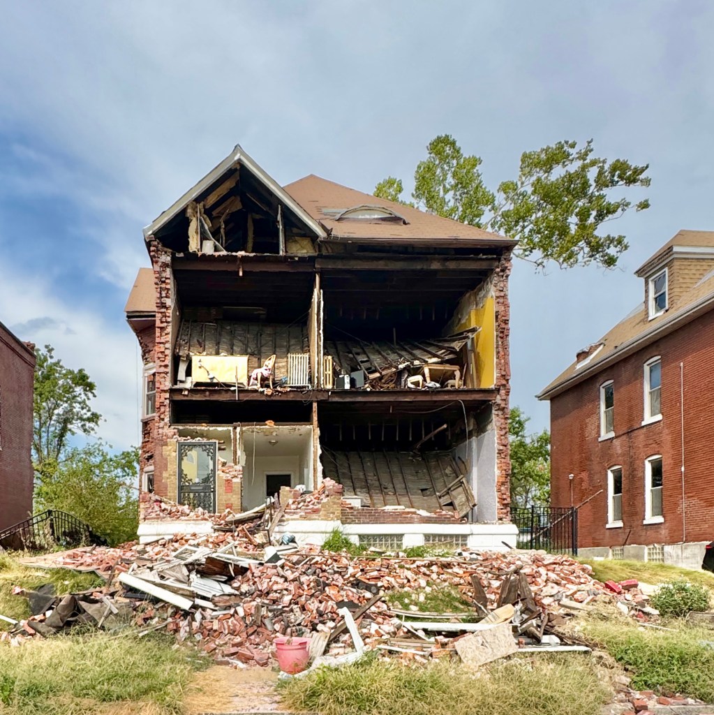 An image of a severely damaged house with exposed interior and debris in front, showing the impact of a tornado.