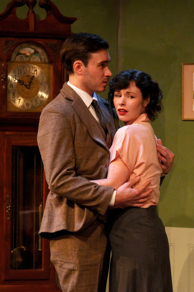 A scene from the play **_I Have Been Here Before_** featuring a man in a suit and a woman in a blouse, standing closely together in a domestic setting, expressing a moment of intimacy.