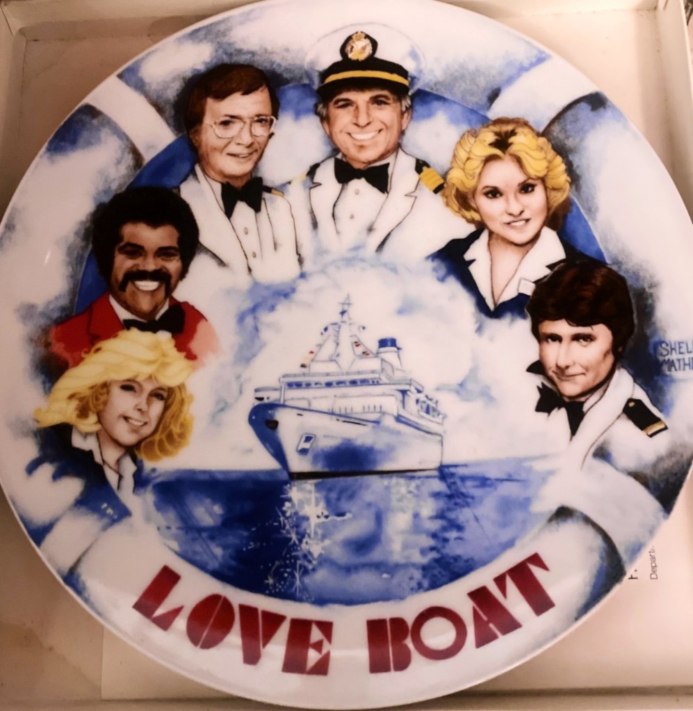 A decorative plate featuring characters from the television show 'Love Boat', with a depiction of a cruise ship and the show's title at the bottom.