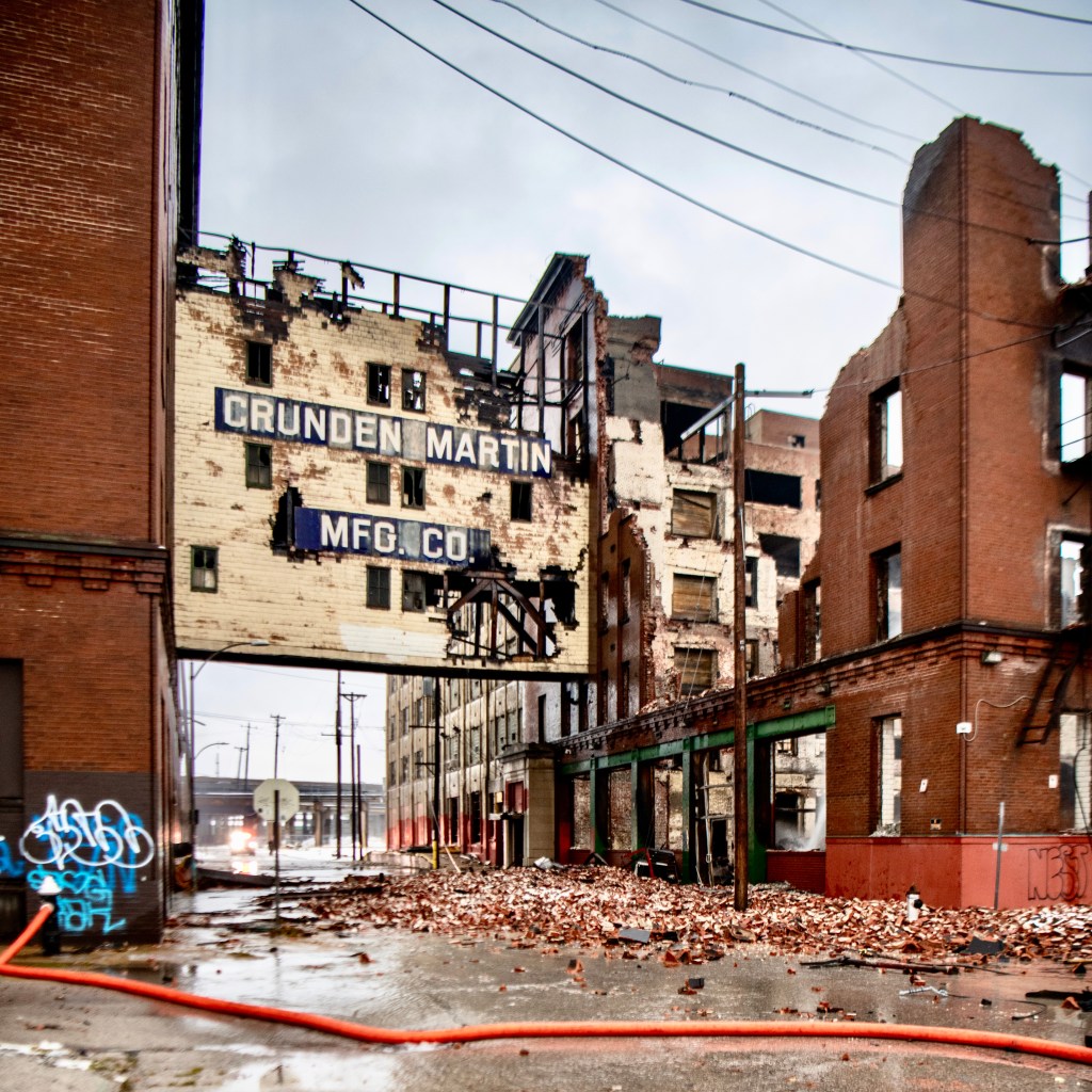 Ruined Crunden-Martin Manufacturing Company warehouse, with brick walls and a sign partially intact, amid debris on the ground after a devastating fire.