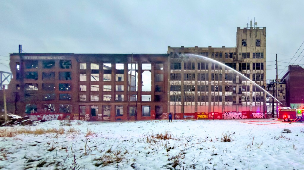 Firefighters battling a large fire at the Crunden-Martin Manufacturing Company warehouses, with smoke rising from the red-brick structure and covered in snow.