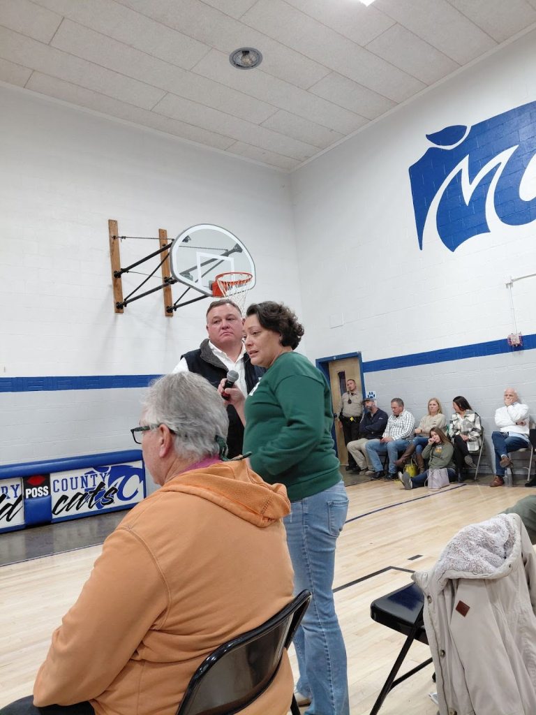 A community meeting at Montgomery City Elementary School with several attendees, where residents express concerns about proposed data centers. A woman speaks into a microphone while a man listens.