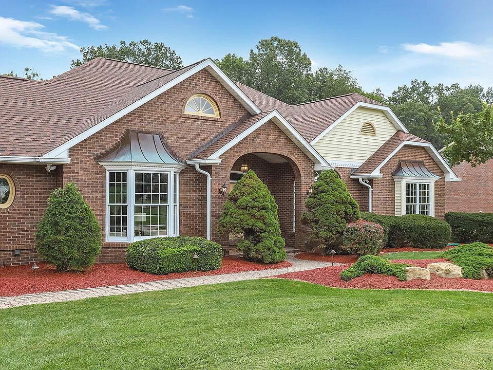 A brick house featuring a landscaped front yard with green shrubs and red mulch, complemented by a clear blue sky.