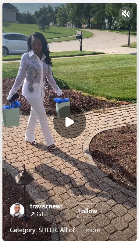 A woman in a stylish outfit walking on a stone pathway, carrying two gift bags, with a grassy area and houses in the background.