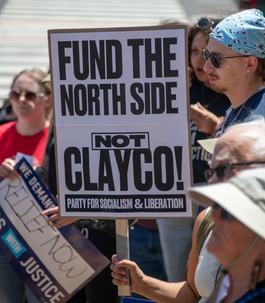 Protesters holding signs at a rally, with a prominent sign reading 'FUND THE NORTH SIDE NOT CLAYCO! PARTY FOR SOCIALISM & LIBERATION'.