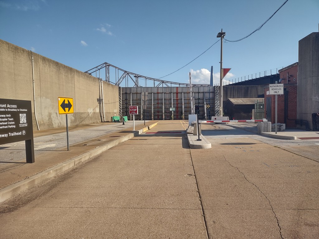A view of a concrete access road leading to a barrier gate, with directional signs for authorized vehicles and waterfront access.