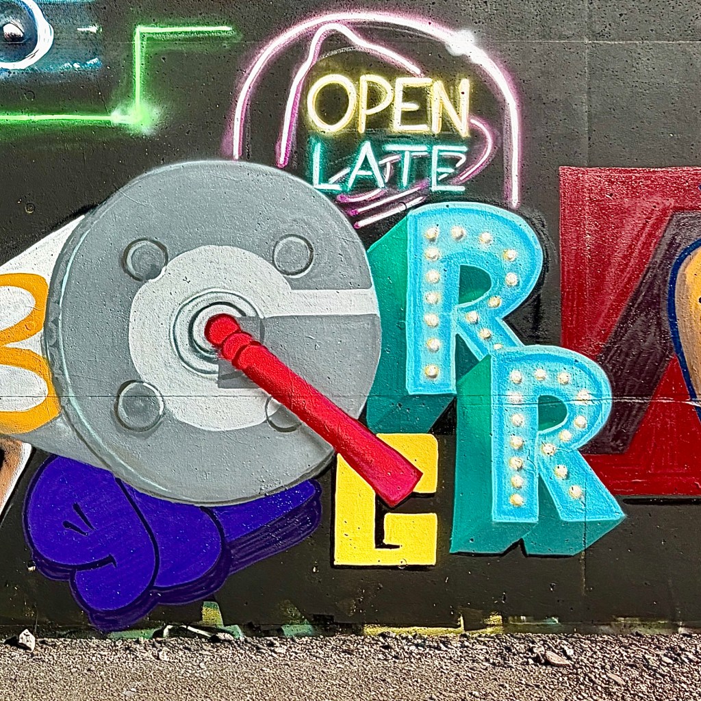A vibrant mural featuring a colorful megaphone and the words 'Open Late' in neon lights, with various artistic letters and designs in the background.