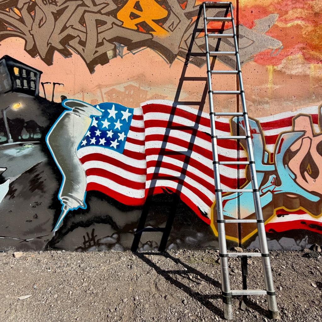 A metallic ladder positioned against a colorful graffiti wall featuring an American flag design with vibrant colors and textures.