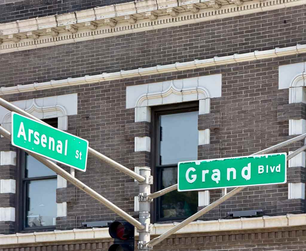 Street signs for Arsenal Street and Grand Boulevard at an intersection against a brick building.