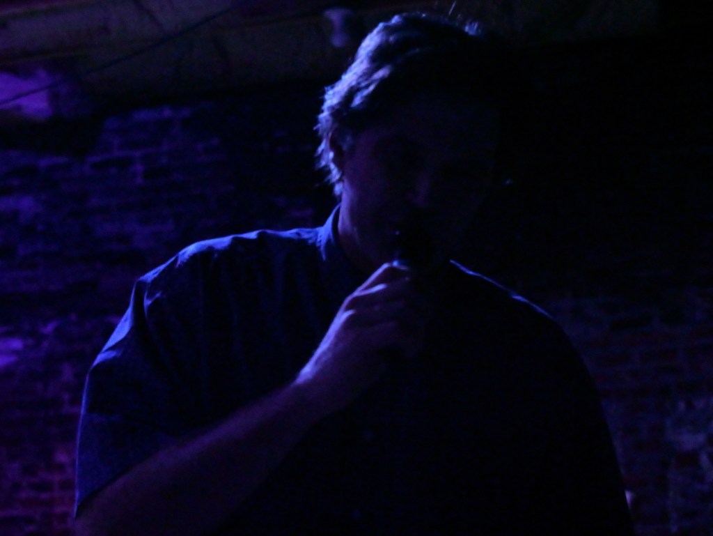 A person holding a microphone in a dimly lit space with purple lighting, creating a shadowy effect.
